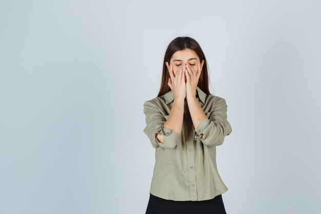 Young lady keeping hands on face in shirt, skirt and looking unwell