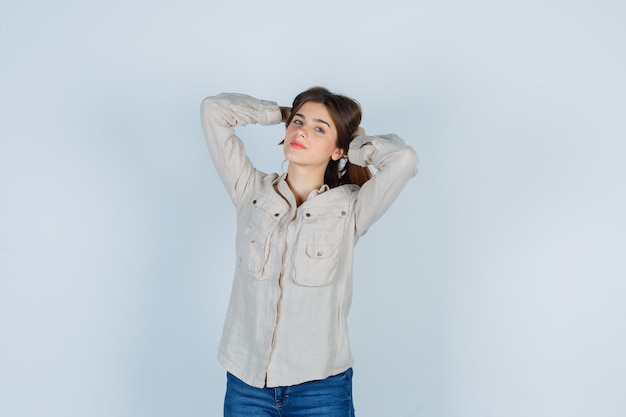 Young lady keeping hands behind head in casual, jeans and looking relaxed , front view.