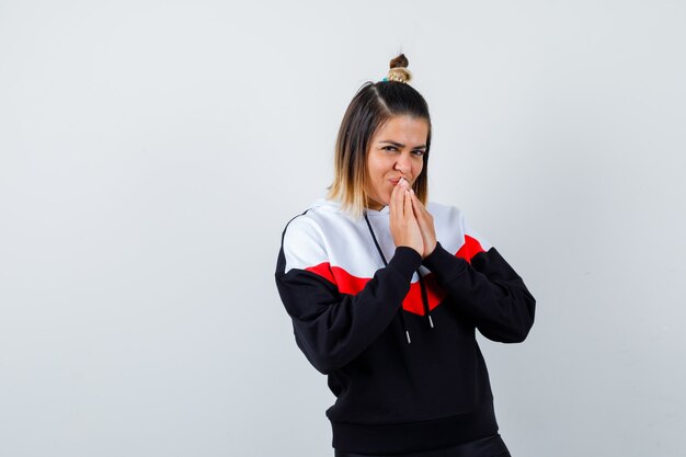 Young lady keeping hands on mouth in hoodie sweater and looking joyful