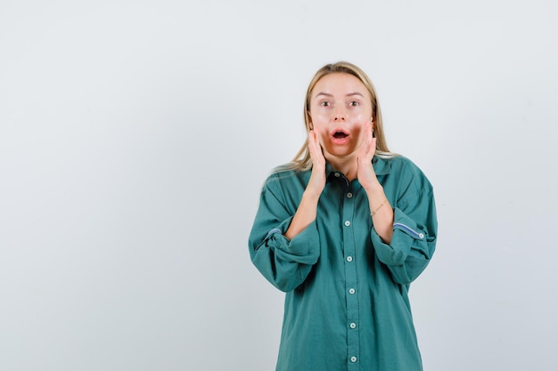 Young lady keeping hands near open mouth in green shirt and looking shocked