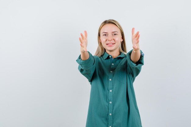 Young lady keeping hands outstretched in green shirt and looking cheerful