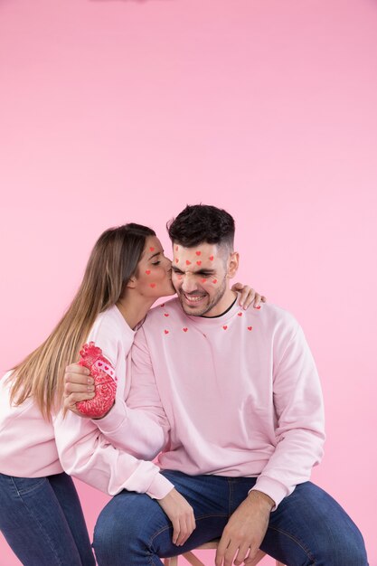 Young lady kissing smiling guy with paper hearts on faces