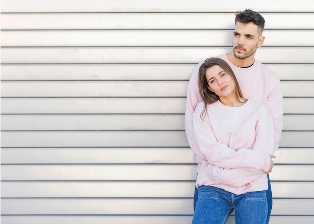 Young lady leaning on bearded guy near corrugated metal