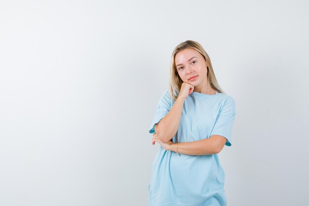 Young lady leaning cheek on fist in t-shirt and looking thoughtful isolated