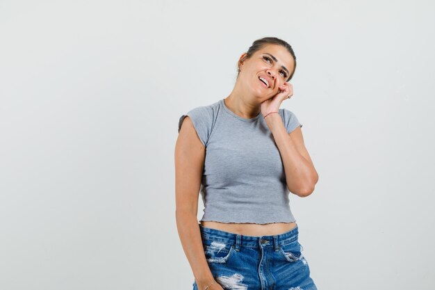 Young lady leaning cheek on hand in t-shirt, shorts and looking dreamy. 