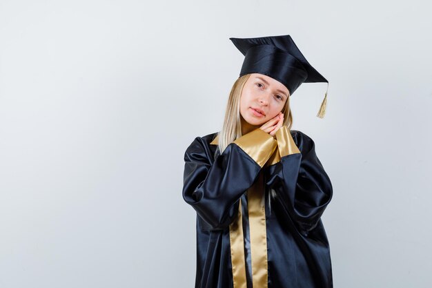 Young lady leaning cheek on hands in academic dress and looking sleepy.