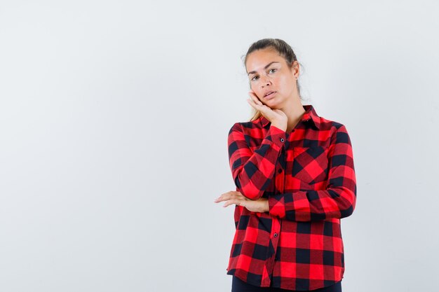Young lady leaning cheek on palm in checked shirt and looking cute