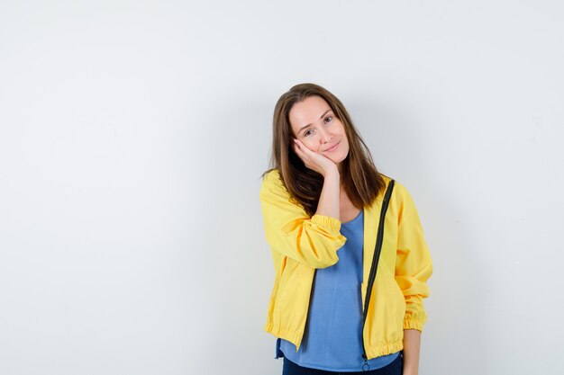 Young lady leaning cheek on palm in t-shirt, jacket and looking cute. front view.