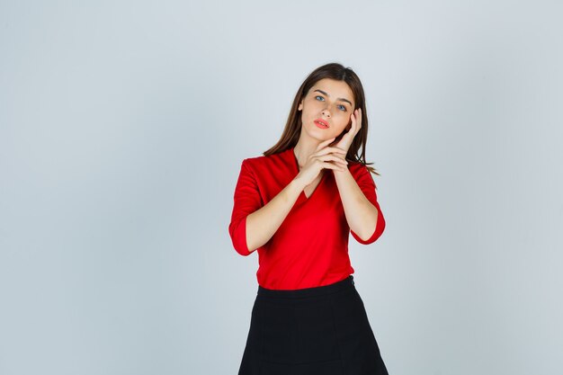 Young lady leaning cheek on palm while posing in red blouse