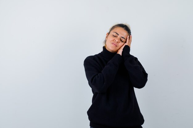 Young lady leaning on hands as pillow in black sweater and looking sleepy. front view.