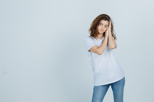 Giovane donna che si appoggia sulle mani come cuscino in t-shirt, jeans e sembra assonnata. vista frontale.