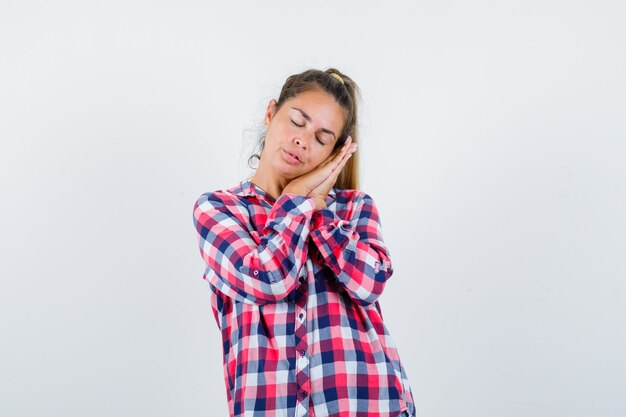 Young lady leaning on palms as pillow in checked shirt and looking peaceful , front view.