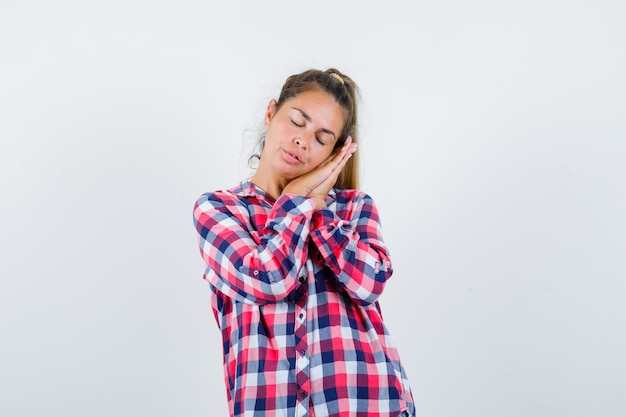 Young lady leaning on palms as pillow in checked shirt and looking peaceful , front view.