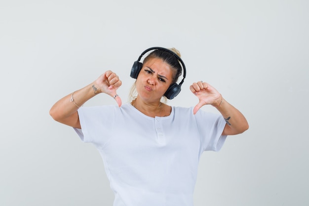 Young lady listening to music, showing double thumbs down in t-shirt , front view.