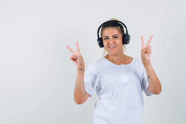 Young lady listening to music, showing v-sign in t-shirt , front view.