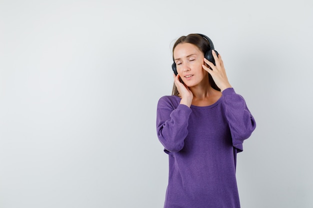 Молодая леди, слушающая музыку в наушниках в фиолетовой рубашке и восхитительно выглядящая, вид спереди.