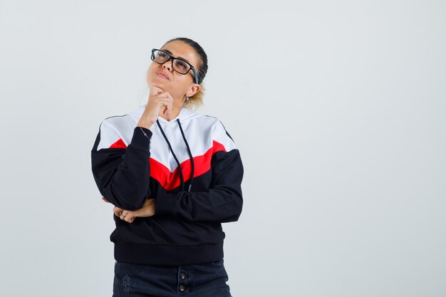 Young lady looking away in colorful sweatshirt,glasses and looking pensive. front view. 