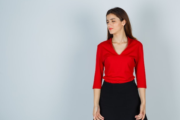 Young lady looking away in red blouse, skirt and looking pensive