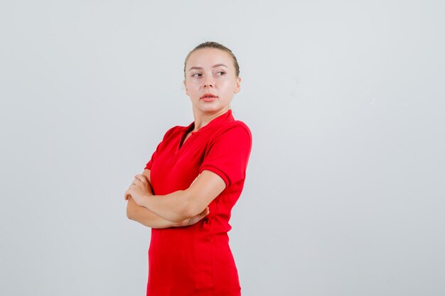 Young lady looking away with crossed arms in red t-shirt and looking confident
