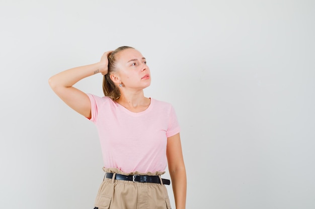 Tシャツとズボンで頭を抱えて目をそらし、物思いにふける若い女性