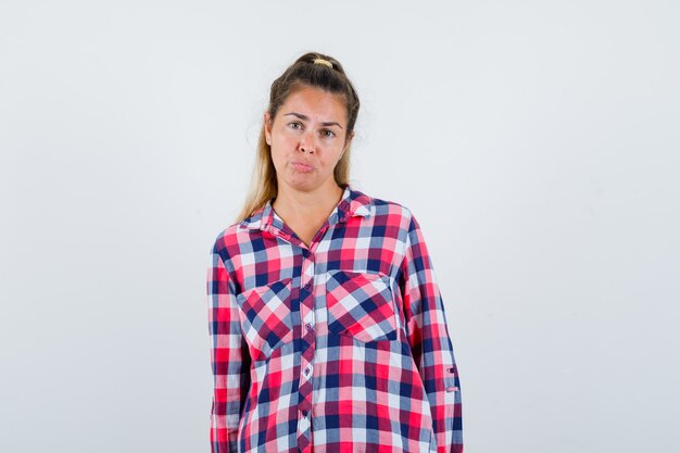 Young lady looking at camera in checked shirt and looking helpless. front view.