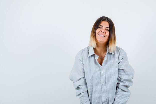 Young lady looking at camera in oversize shirt and looking joyful , front view.