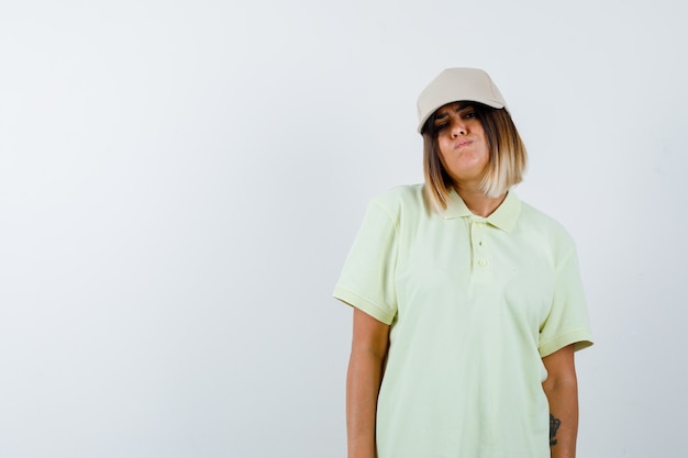 Free photo young lady looking at camera in t-shirt, cap and looking wistful , front view.