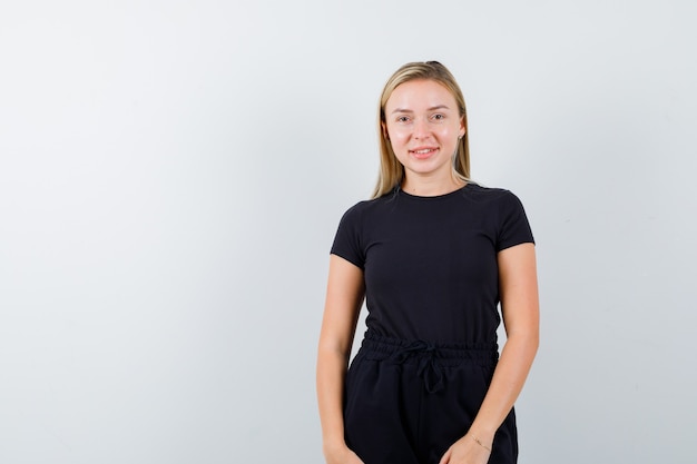 Foto gratuita giovane donna che guarda l'obbiettivo in t-shirt, pantaloni e che sembra gioiosa. vista frontale.