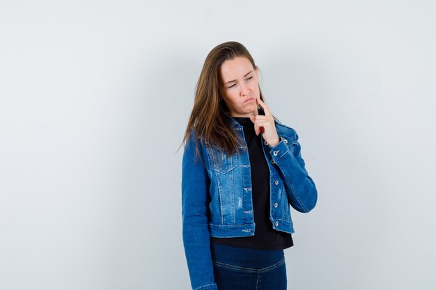 Young lady looking down while thinking in blouse and looking hesitant. front view.