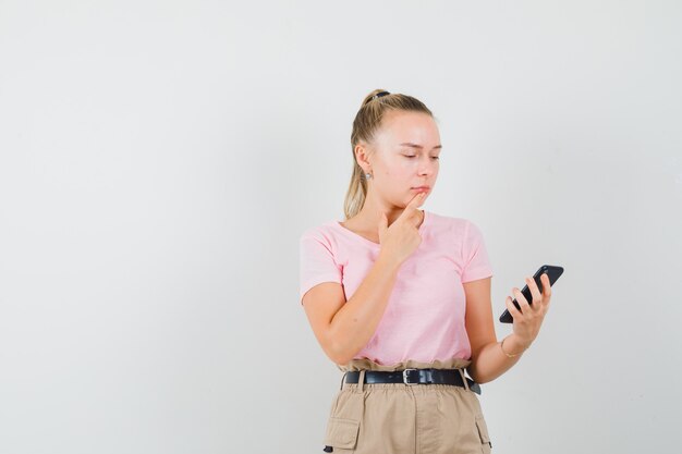 Young lady looking at mobile phone in t-shirt and pants and looking pensive