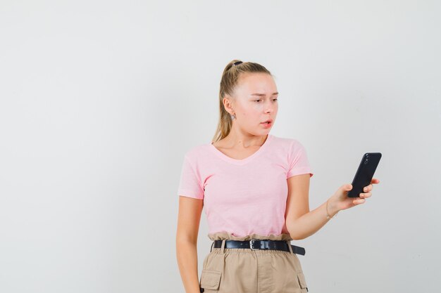 Young lady looking at mobile phone in t-shirt and pants and looking puzzled