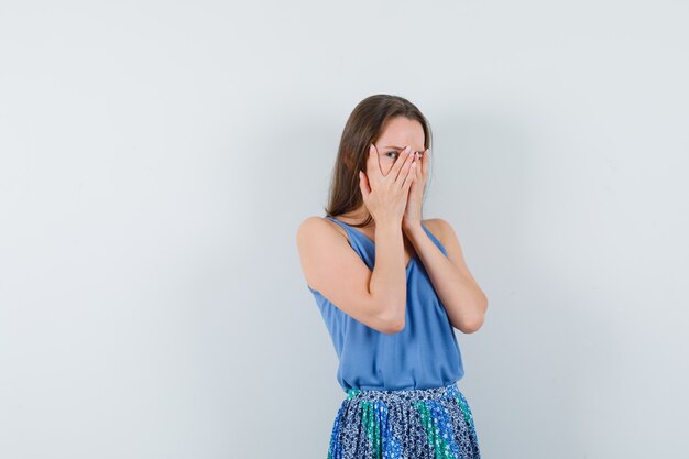 Young lady looking through fingers in blouse,skirt and looking excited , front view.