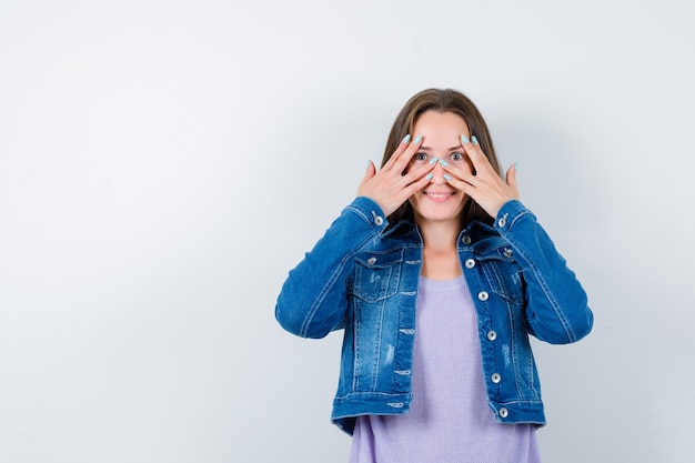 Free photo young lady looking through fingers in t-shirt, jacket and looking cheerful. front view.