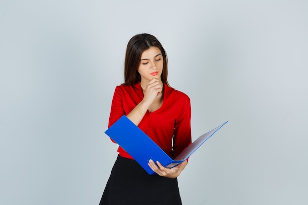 Young lady looking through folder in red blouse, skirt and looking focused