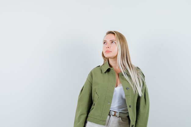 Young lady looking up in jacket, pants and looking pensive. front view.