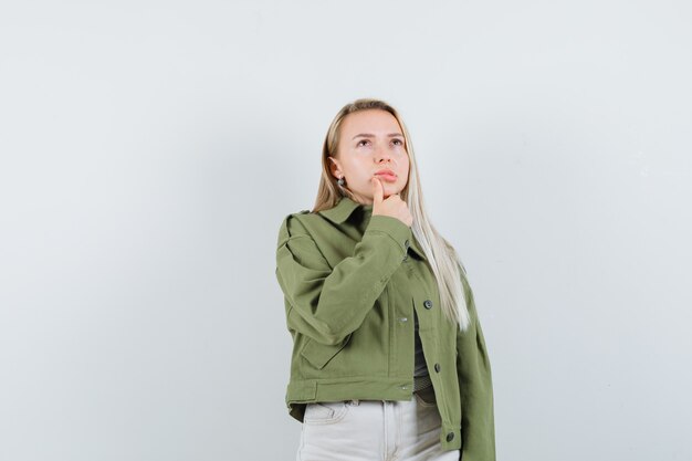 Young lady looking up in jacket, pants and looking pensive , front view.