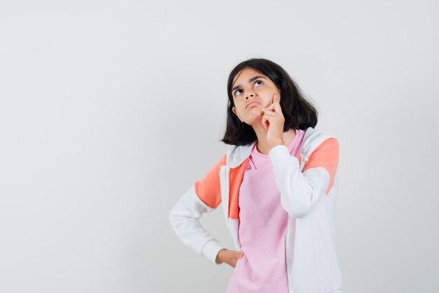 Young lady looking up in jacket, pink shirt and looking thoughtful.