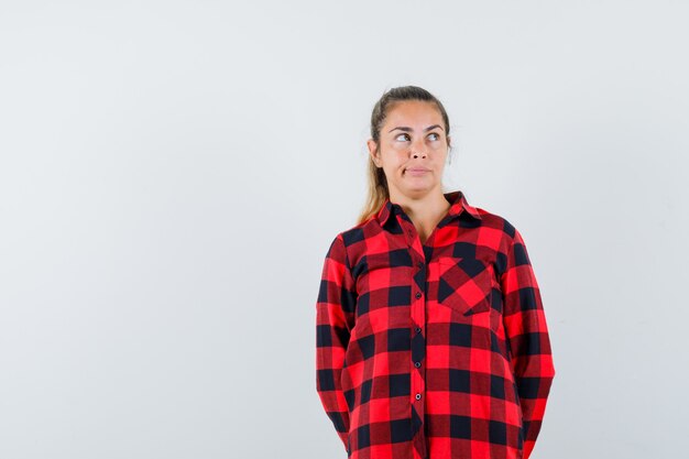 Young lady looking up while thinking in checked shirt and looking forgetful