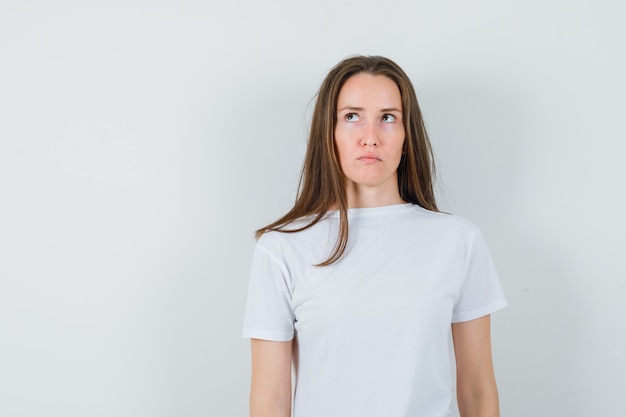 Young lady looking up in white t-shirt and looking hesitant 