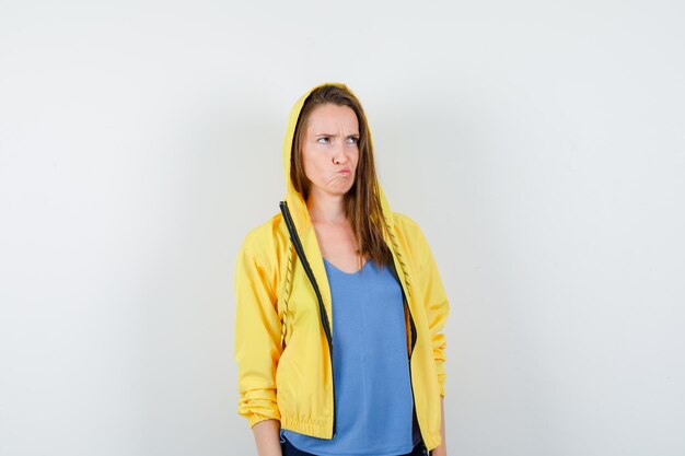 Young lady looking upward while scowling in t-shirt, jacket and looking hesitant