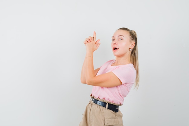 Young lady making finger pistol sign in t-shirt and pants and looking confident