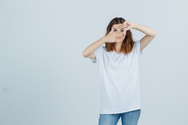 若い女性がTシャツ、ジーンズでフレームジェスチャーを作成し、嬉しそうに見える、正面図。