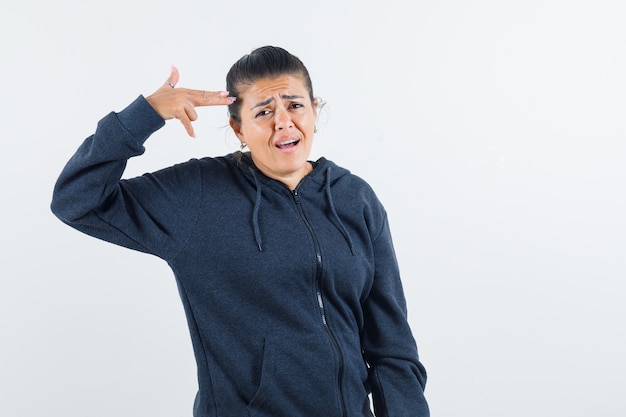 Young lady making pistol gesture on head in jacket and looking bored 