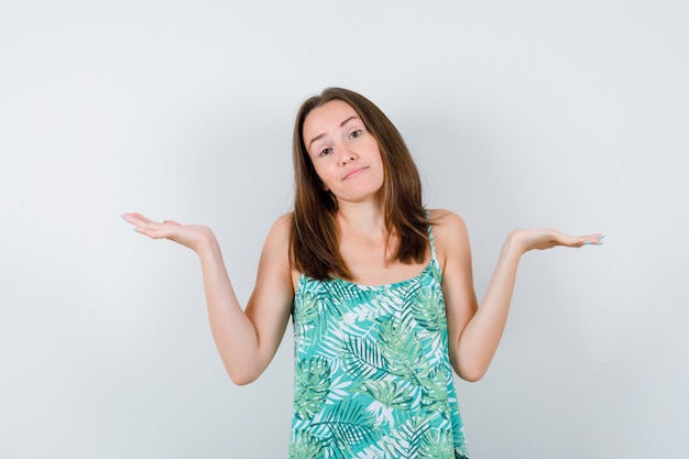 Young lady making scales gesture in blouse and looking hesitant , front view.