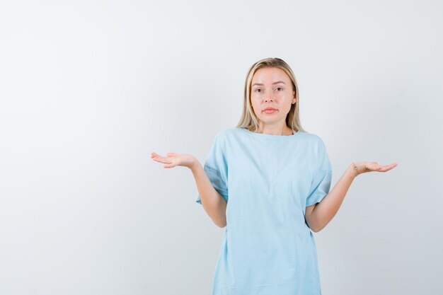 Young lady making scales gesture in t-shirt and looking hesitant isolated