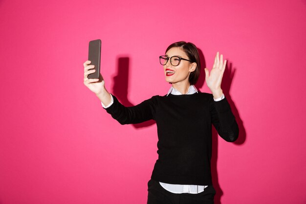 分離されたスマートフォンでselfieを作る若い女性