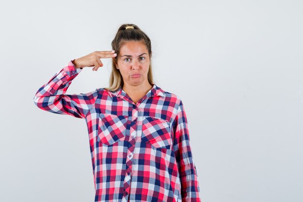 Young lady making suicide gesture in checked shirt and looking confident , front view.