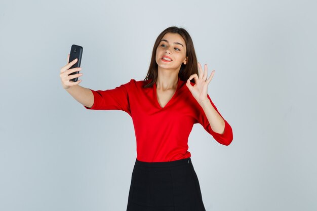 Молодая дама делает видеозвонок, показывая жест в красной блузке