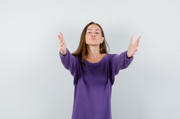 Young lady opening arms for hug and kiss in violet shirt front view.