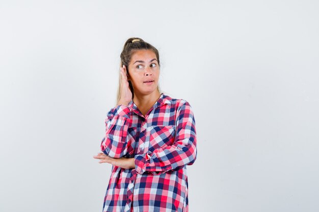 Young lady overhearing private conversation in checked shirt and looking curious. front view.